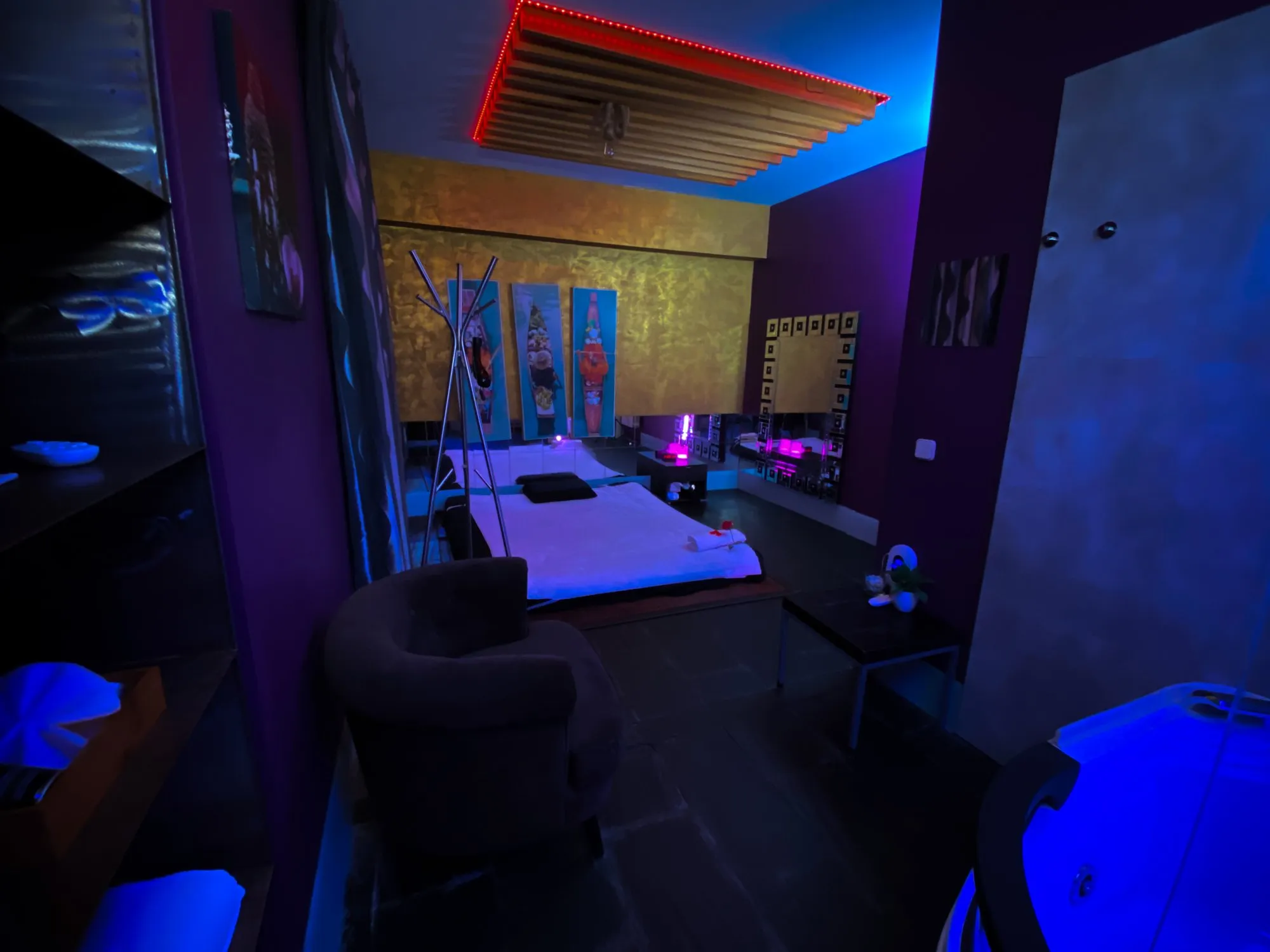 Jacuzzi iluminado, luz azul y morada y una pared dorada con tres cuadros.